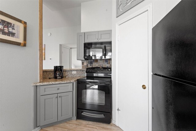 kitchen with light stone counters, tasteful backsplash, black appliances, light wood-style flooring, and gray cabinetry