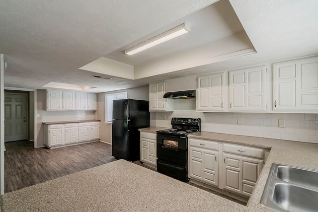 kitchen with under cabinet range hood, a raised ceiling, a sink, backsplash, and black appliances