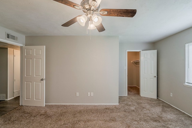 unfurnished bedroom with a walk in closet, carpet flooring, baseboards, and visible vents