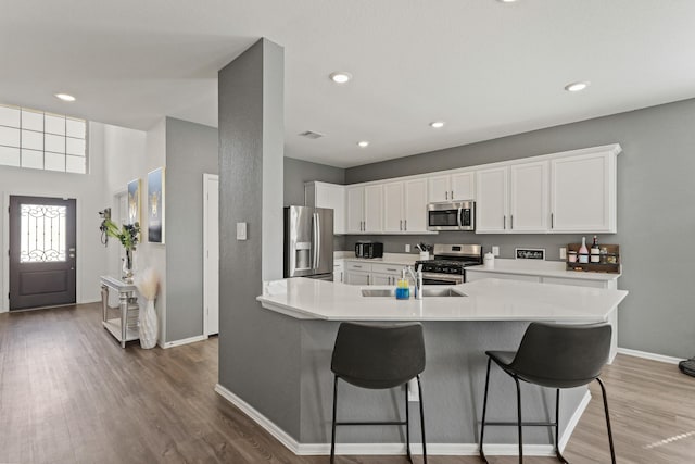 kitchen with a kitchen breakfast bar, a sink, stainless steel appliances, baseboards, and wood finished floors