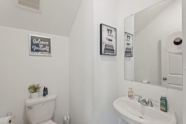 half bath with lofted ceiling, visible vents, toilet, and a sink