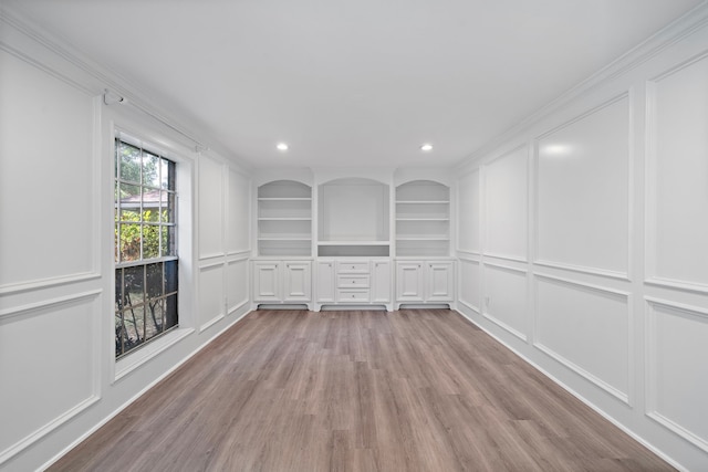 empty room with recessed lighting, light wood-style floors, a decorative wall, and crown molding