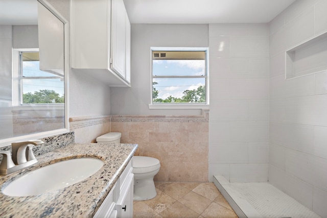 full bathroom with a tile shower, tile walls, wainscoting, toilet, and vanity