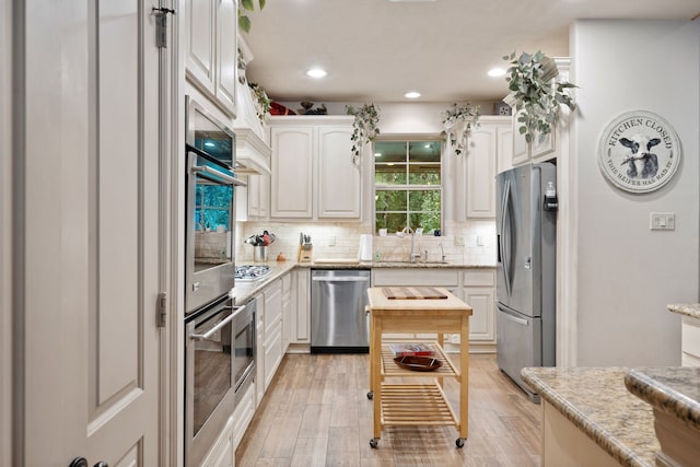25672 Magnolia Pines Dr, Magnolia, TX 77355 - kitchen featuring stainless steel appliances, a sink, tasteful backsplash, light wood-type flooring, and white cabinetry