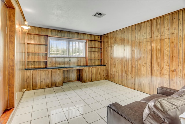 unfurnished room with wood walls, visible vents, built in shelves, and light tile patterned floors