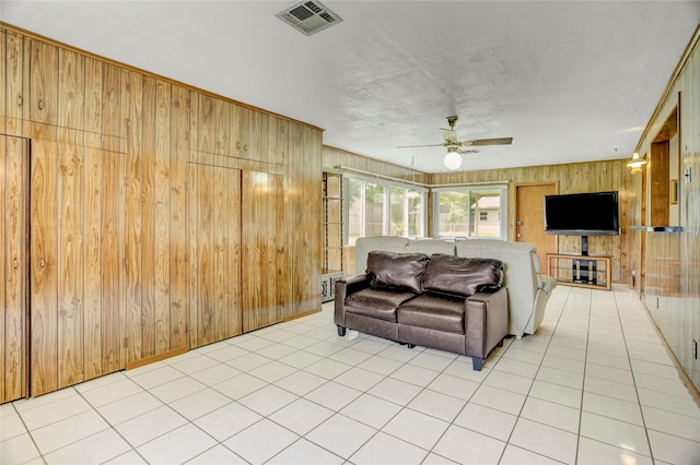living area with wooden walls, visible vents, a ceiling fan, and light tile patterned flooring
