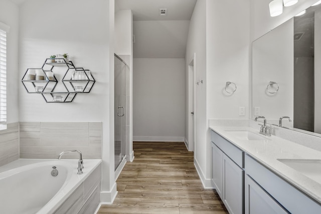 bathroom with a garden tub, a shower stall, double vanity, wood finished floors, and baseboards