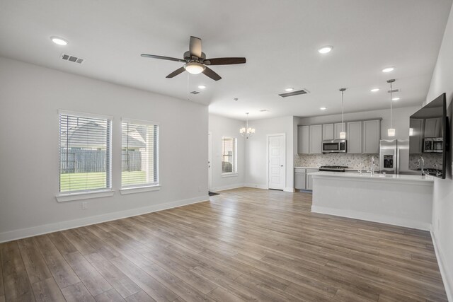 unfurnished living room featuring ceiling fan, a chandelier, light wood-type flooring, baseboards, and recessed lighting