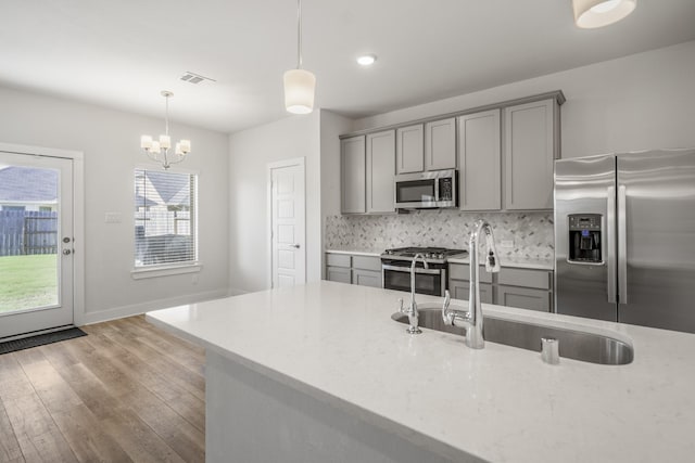 kitchen featuring gray cabinetry, stainless steel appliances, a sink, light wood-type flooring, and decorative light fixtures