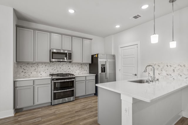 kitchen featuring appliances with stainless steel finishes, gray cabinetry, a sink, backsplash, and recessed lighting