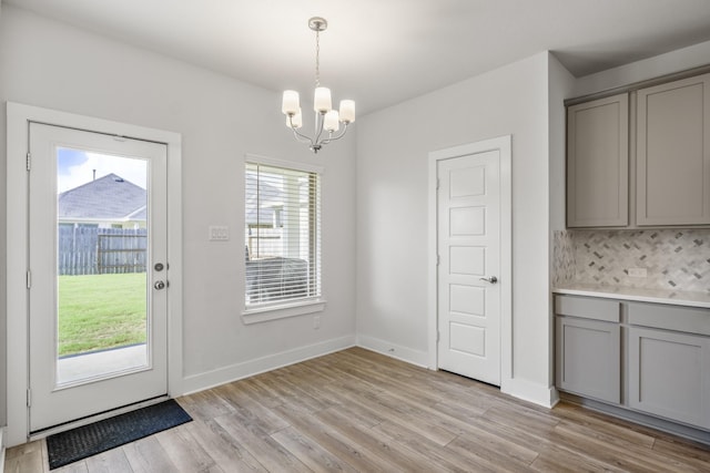 doorway with a chandelier, light wood-type flooring, and baseboards