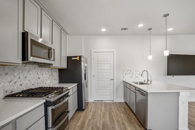 kitchen featuring appliances with stainless steel finishes, a sink, gray cabinets, a peninsula, and light wood-style floors
