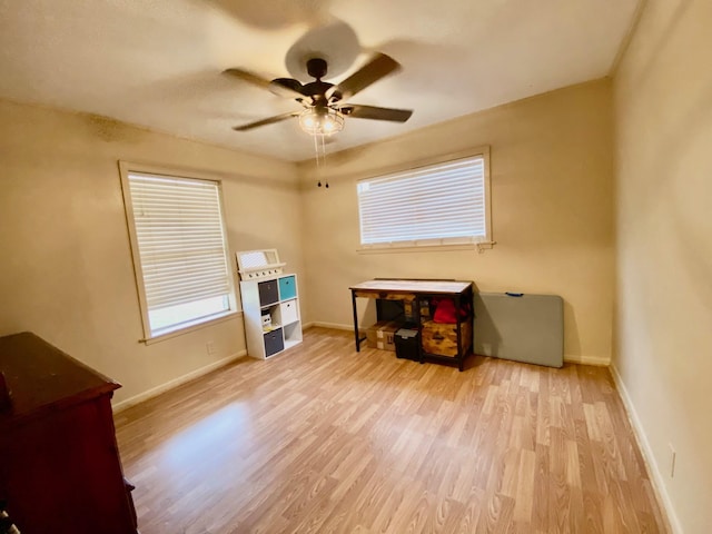 misc room with baseboards, a ceiling fan, wood finished floors, and a healthy amount of sunlight