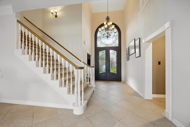 tiled entryway featuring a notable chandelier, stairs, a towering ceiling, baseboards, and ornamental molding