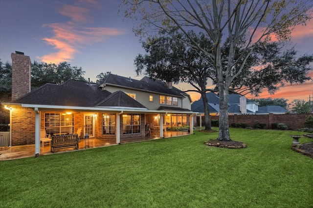 rear view of house with a lawn, fence, a chimney, and brick siding