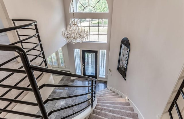 foyer entrance featuring baseboards, a towering ceiling, stairs, and an inviting chandelier