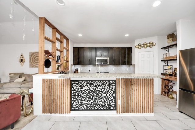 kitchen featuring light stone counters, open shelves, dark brown cabinets, tasteful backsplash, and appliances with stainless steel finishes