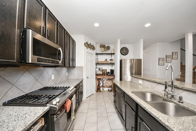 kitchen with tasteful backsplash, a sink, light tile patterned floors, stainless steel appliances, and light stone countertops