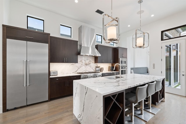 2703 Westgrove Ln, Houston, TX 77027 - kitchen featuring light wood-style floors, built in appliances, backsplash, wall chimney exhaust hood, and visible vents