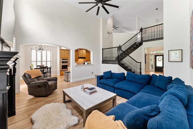 living area featuring high vaulted ceiling, arched walkways, light wood-type flooring, stairs, and ceiling fan
