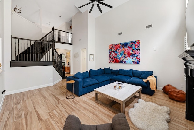 living area featuring visible vents, baseboards, a towering ceiling, stairway, and ceiling fan