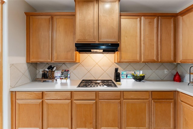 kitchen with stainless steel gas stovetop, light countertops, under cabinet range hood, and backsplash