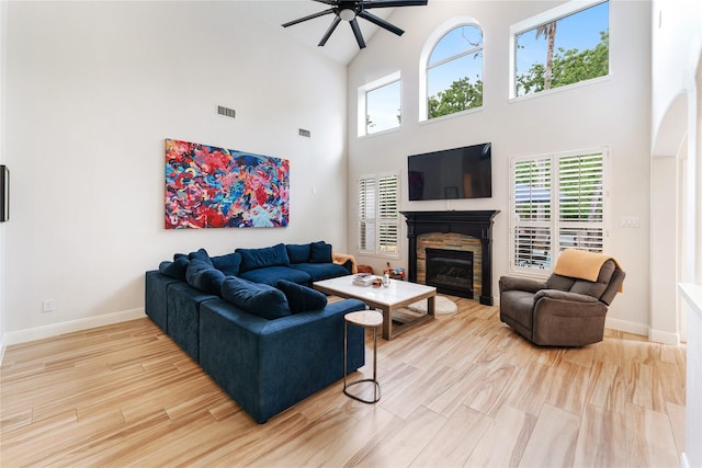 living area with wood finished floors, a ceiling fan, baseboards, a glass covered fireplace, and high vaulted ceiling