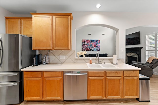 kitchen with a sink, open floor plan, stainless steel appliances, light wood finished floors, and a fireplace