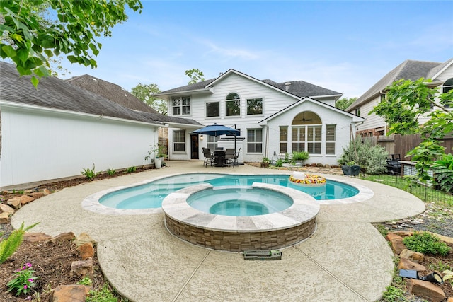 rear view of property featuring fence, outdoor dining space, a patio area, brick siding, and a pool with connected hot tub