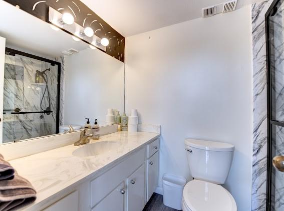 full bathroom with toilet, visible vents, a marble finish shower, and vanity