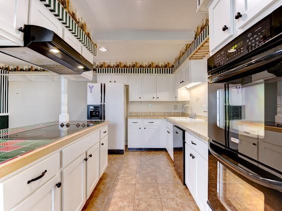 kitchen featuring a sink, light tile patterned floors, white cabinets, black appliances, and under cabinet range hood