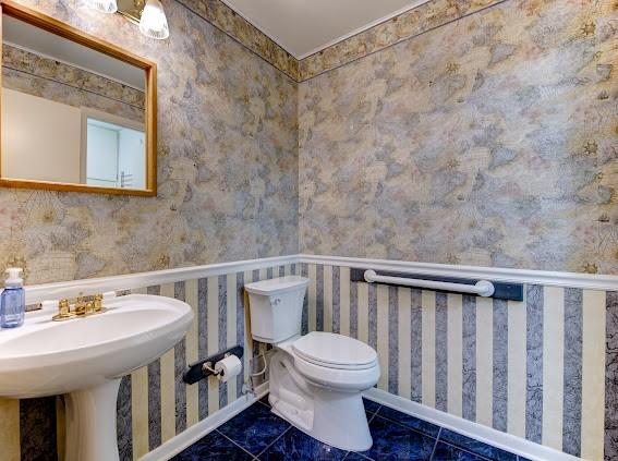 bathroom with baseboards, toilet, and wallpapered walls