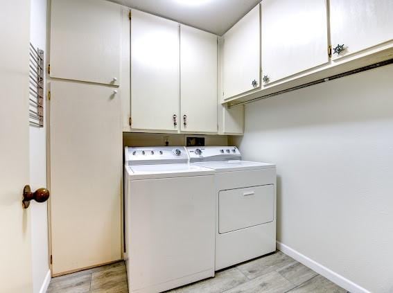 washroom with baseboards, light wood-style flooring, cabinet space, and washing machine and dryer