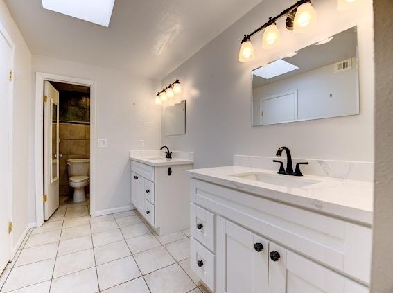 bathroom featuring a sink, tile patterned floors, a skylight, and two vanities