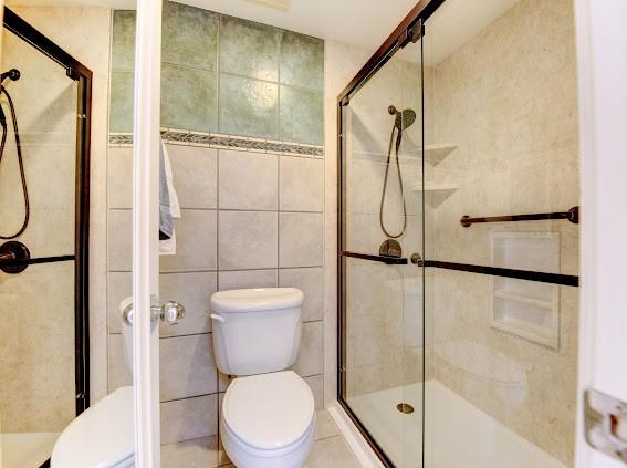 bathroom featuring a shower stall, toilet, and tile walls