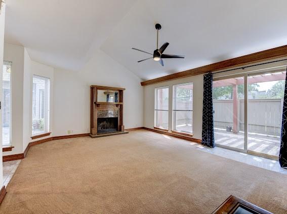 unfurnished living room with a healthy amount of sunlight, a fireplace with raised hearth, a ceiling fan, and light colored carpet