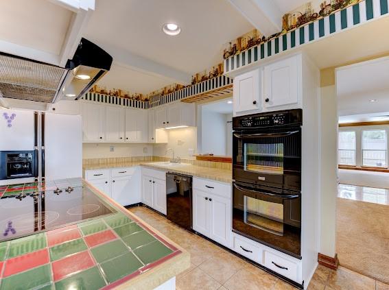 kitchen featuring a sink, white cabinets, light tile patterned floors, and black appliances