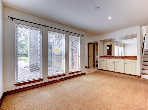 unfurnished living room with baseboards, recessed lighting, stairs, and light carpet