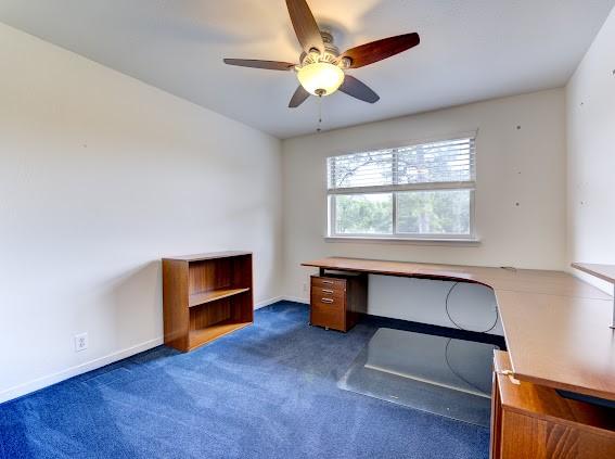 unfurnished office with carpet floors, a ceiling fan, and baseboards