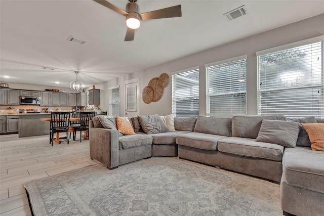 living room with plenty of natural light, visible vents, and ceiling fan with notable chandelier