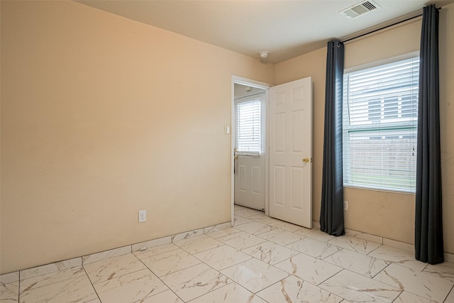 empty room with marble finish floor, baseboards, visible vents, and a wealth of natural light