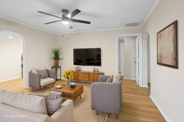 living area featuring arched walkways, light wood-style floors, ornamental molding, a ceiling fan, and baseboards