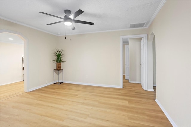 spare room with arched walkways, light wood-type flooring, a ceiling fan, ornamental molding, and baseboards