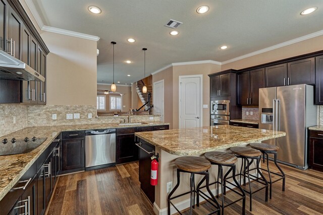 kitchen featuring dark wood-style floors, stainless steel appliances, a sink, light stone countertops, and a kitchen island