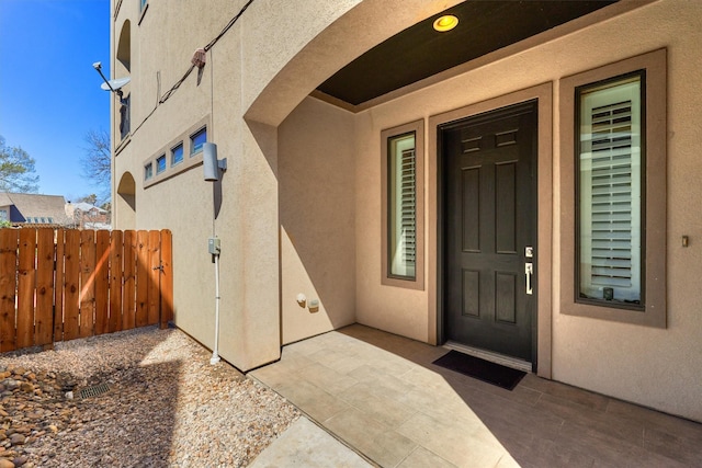 property entrance with stucco siding, fence, and a patio area
