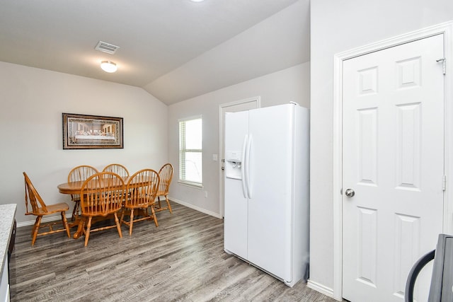 dining space with visible vents, vaulted ceiling, baseboards, and light wood-style flooring