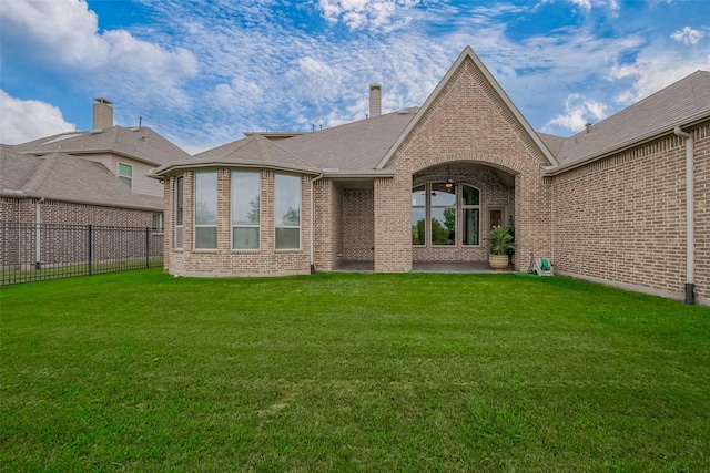 rear view of house featuring fence, a lawn, a chimney, and brick siding