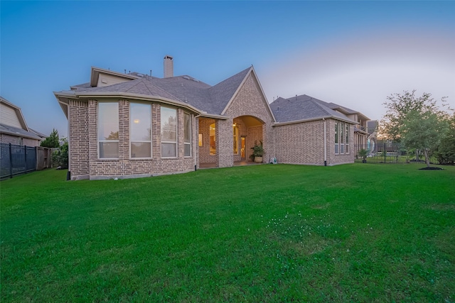 back of property featuring fence, a chimney, brick siding, and a yard