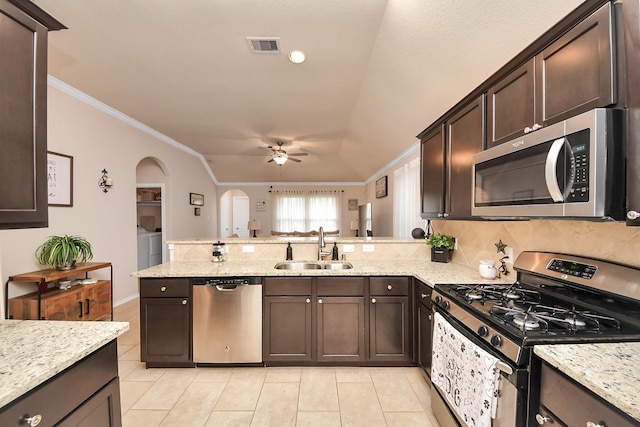 kitchen with a sink, light tile patterned floors, arched walkways, washer and dryer, and appliances with stainless steel finishes