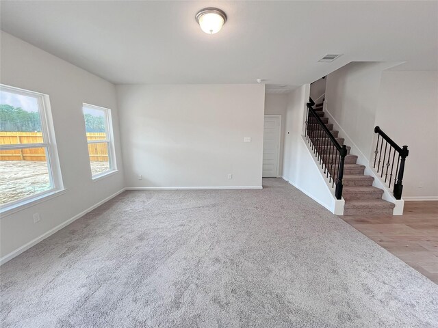 unfurnished living room featuring baseboards, visible vents, stairs, and carpet flooring
